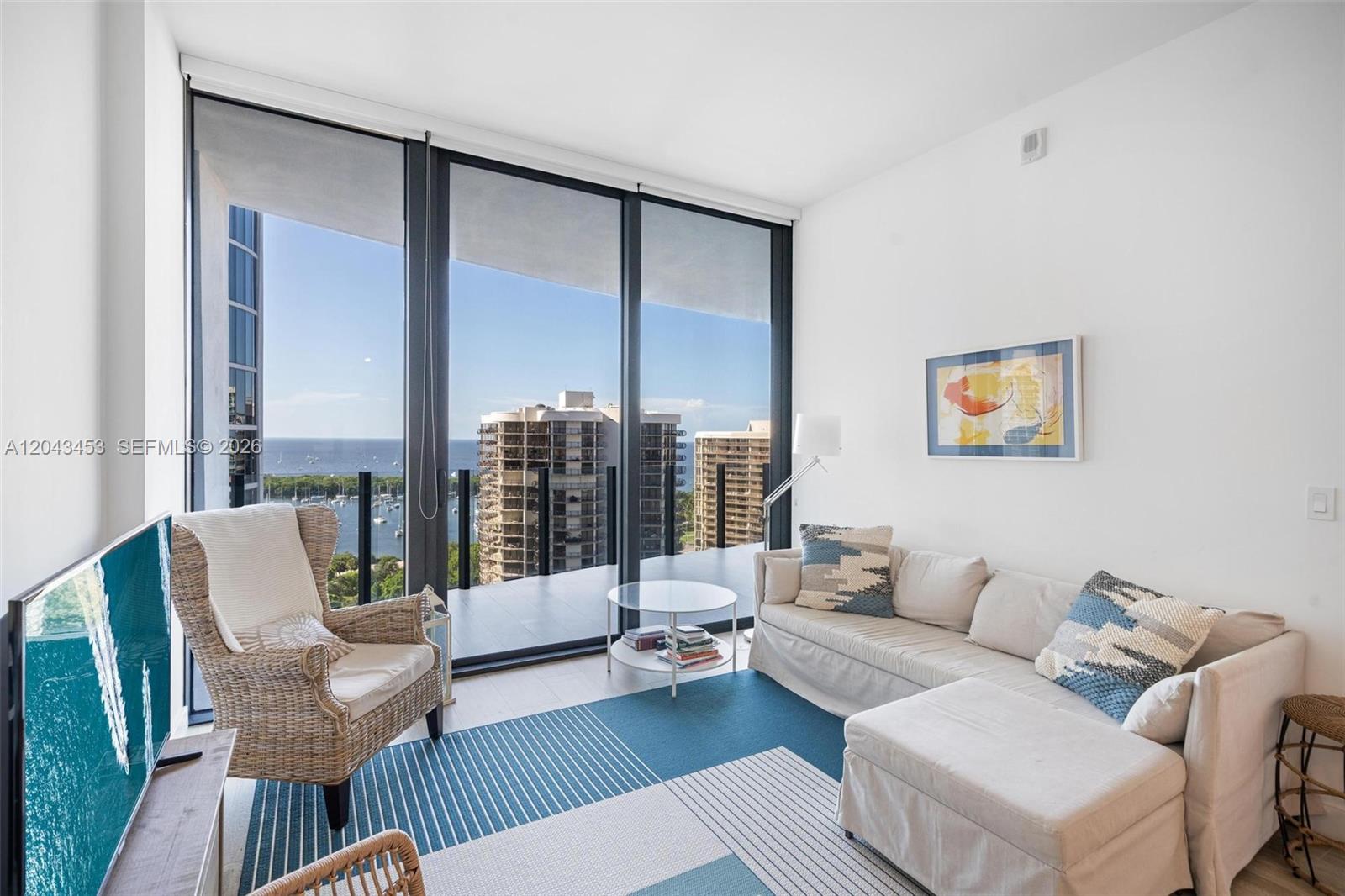 A living room features a wicker chair, sectional sofa, and floor-to-ceiling windows overlooking the ocean — 2831 S Bayshore Dr # 1603, Miami FL 33133, MIAMI, FL