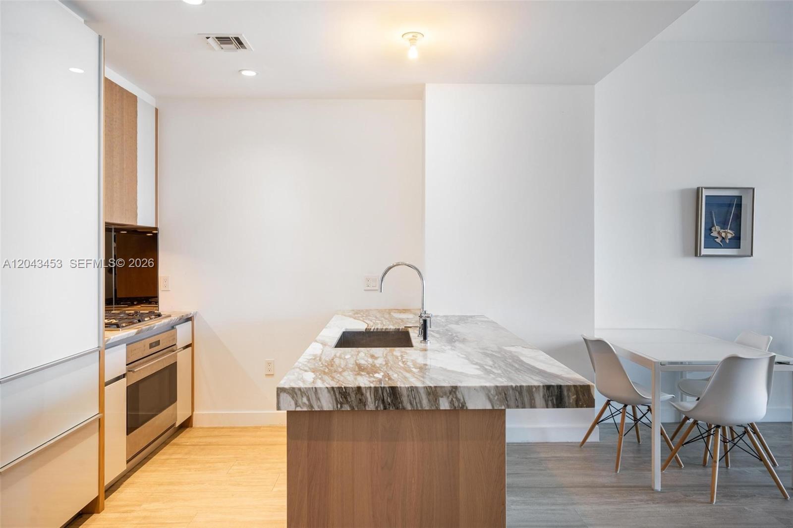 A modern kitchen features a marble-topped island, light wood cabinetry, and an adjacent dining area — 2831 S Bayshore Dr # 1603, Miami FL 33133, MIAMI, FL
