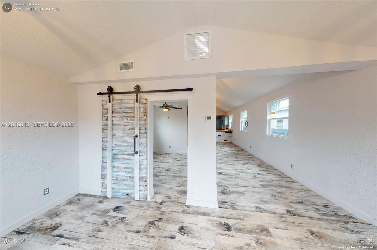A room with wood-look tile flooring features a rustic sliding barn door and vaulted ceilings — 265 NW 80th St, Miami FL 33150, MIAMI, FL