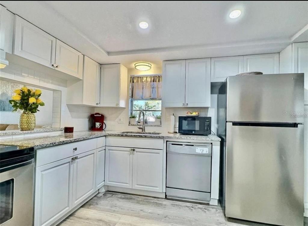 A kitchen with white cabinets, granite countertops, stainless steel appliances, and light wood-look flooring — 8651 10TH STREET N UNIT 130, ST PETERSBURG, FL