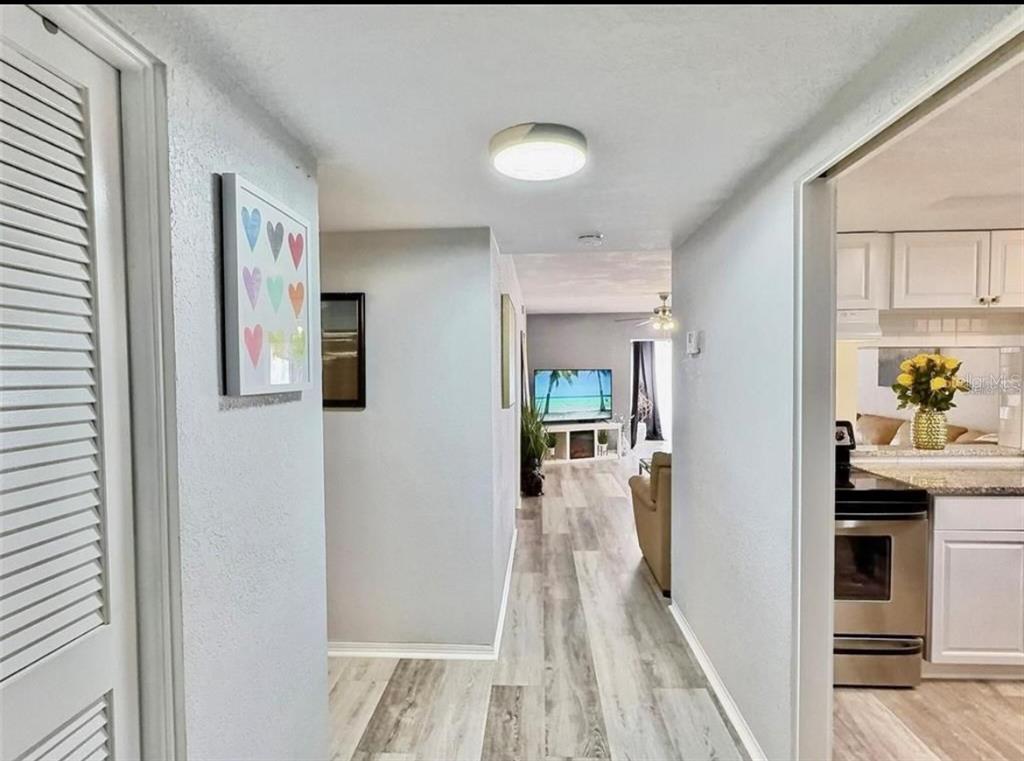 A hallway with light wood-look flooring leads to a living area with a television — 8651 10TH STREET N UNIT 130, ST PETERSBURG, FL