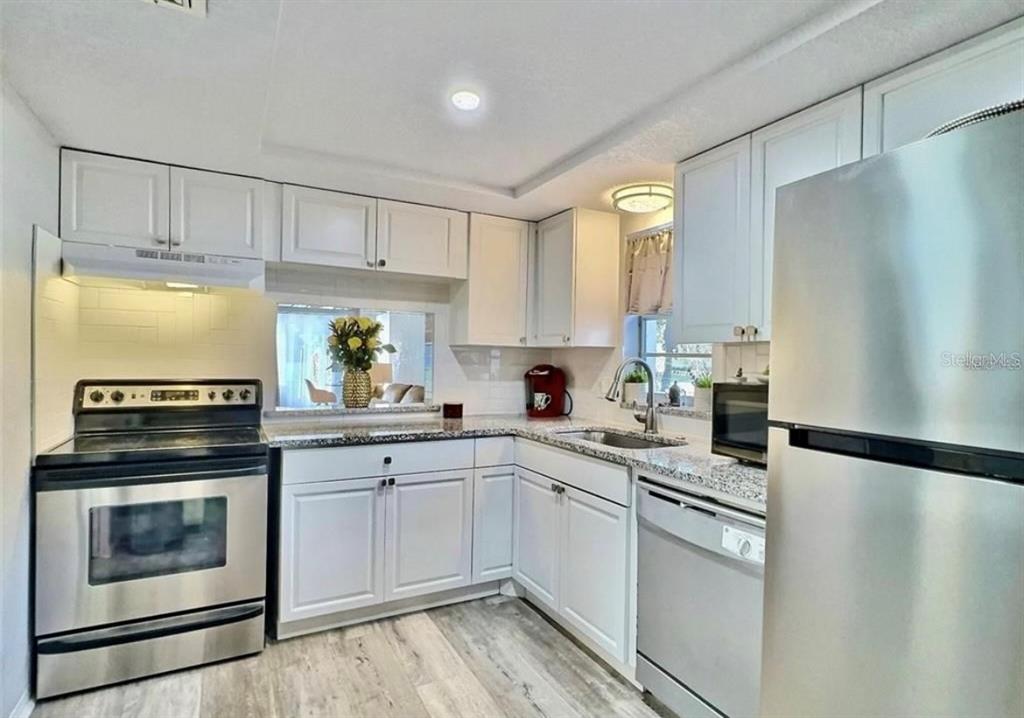 A kitchen features white cabinets, stainless steel appliances, granite countertops, and light wood-look flooring — 8651 10TH STREET N UNIT 130, ST PETERSBURG, FL