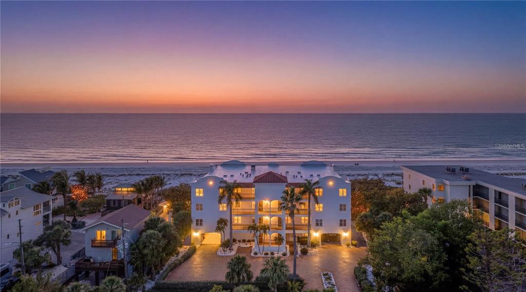 An aerial view of a beachfront condominium building at sunset with a red location pin — 3110 1ST STREET W UNIT 101, ST PETE BEACH, FL