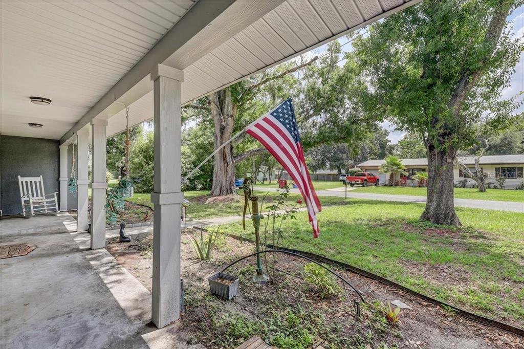 A covered front porch features a white rocking chair and an American flag on display — 903 N BRACEWELL DRIVE, PLANT CITY, FL