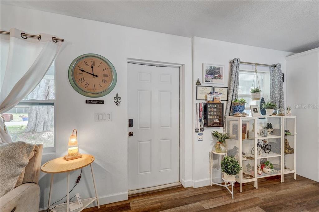 A living room features a white front door, a large wall clock, and a display shelf — 903 N BRACEWELL DRIVE, PLANT CITY, FL