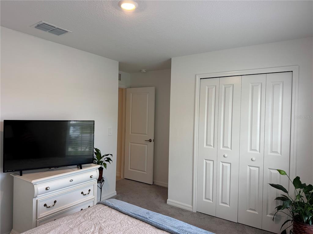 A bedroom features a white dresser with a television, a closet with bifold doors, and carpeted flooring — 12218 RADIANT GEM TRAIL, PARRISH, FL