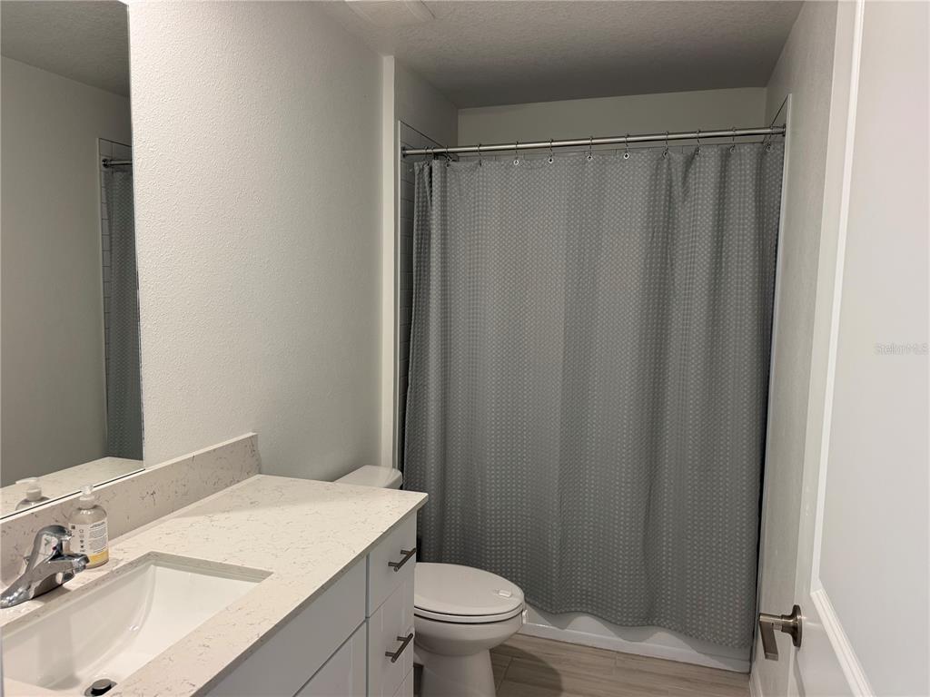 A bathroom features a white vanity with a quartz countertop, a toilet, and a shower — 12218 RADIANT GEM TRAIL, PARRISH, FL