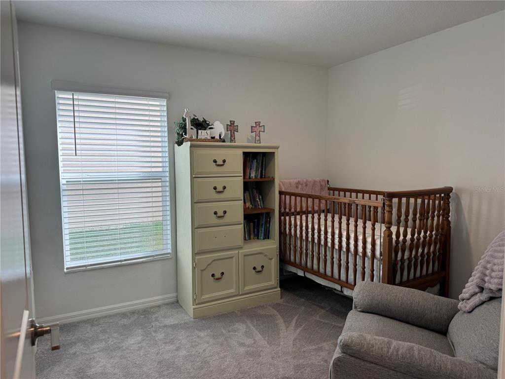 A nursery features a wooden crib, a light-colored dresser with shelving, and a gray armchair — 12218 RADIANT GEM TRAIL, PARRISH, FL