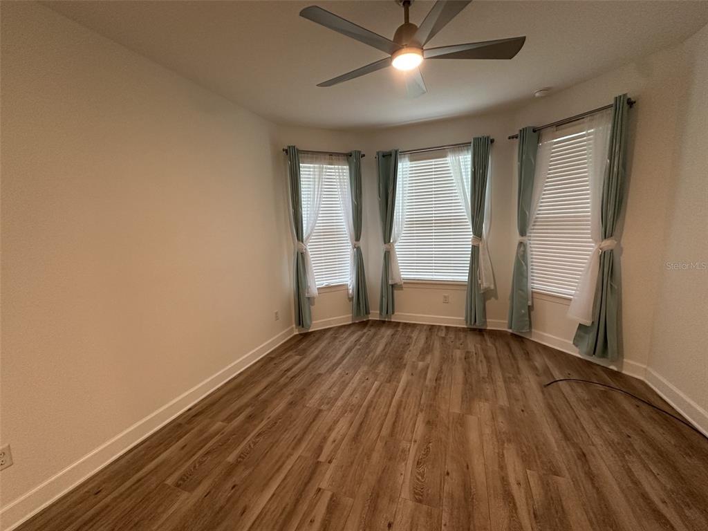 An empty room features wood-look flooring, a ceiling fan, and a bay window with curtains — 1355 ZEEK RIDGE STREET, CLERMONT, FL