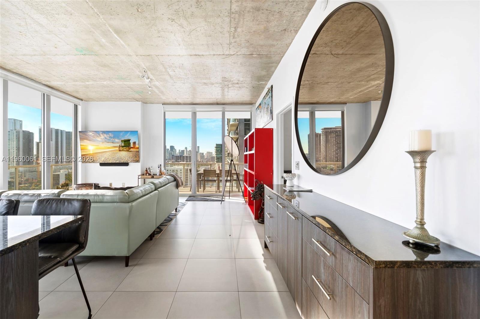 A modern living room features a concrete ceiling, large windows, and a round wall mirror — 3470 E Coast Ave # H2009, Miami FL 33137, MIAMI, FL