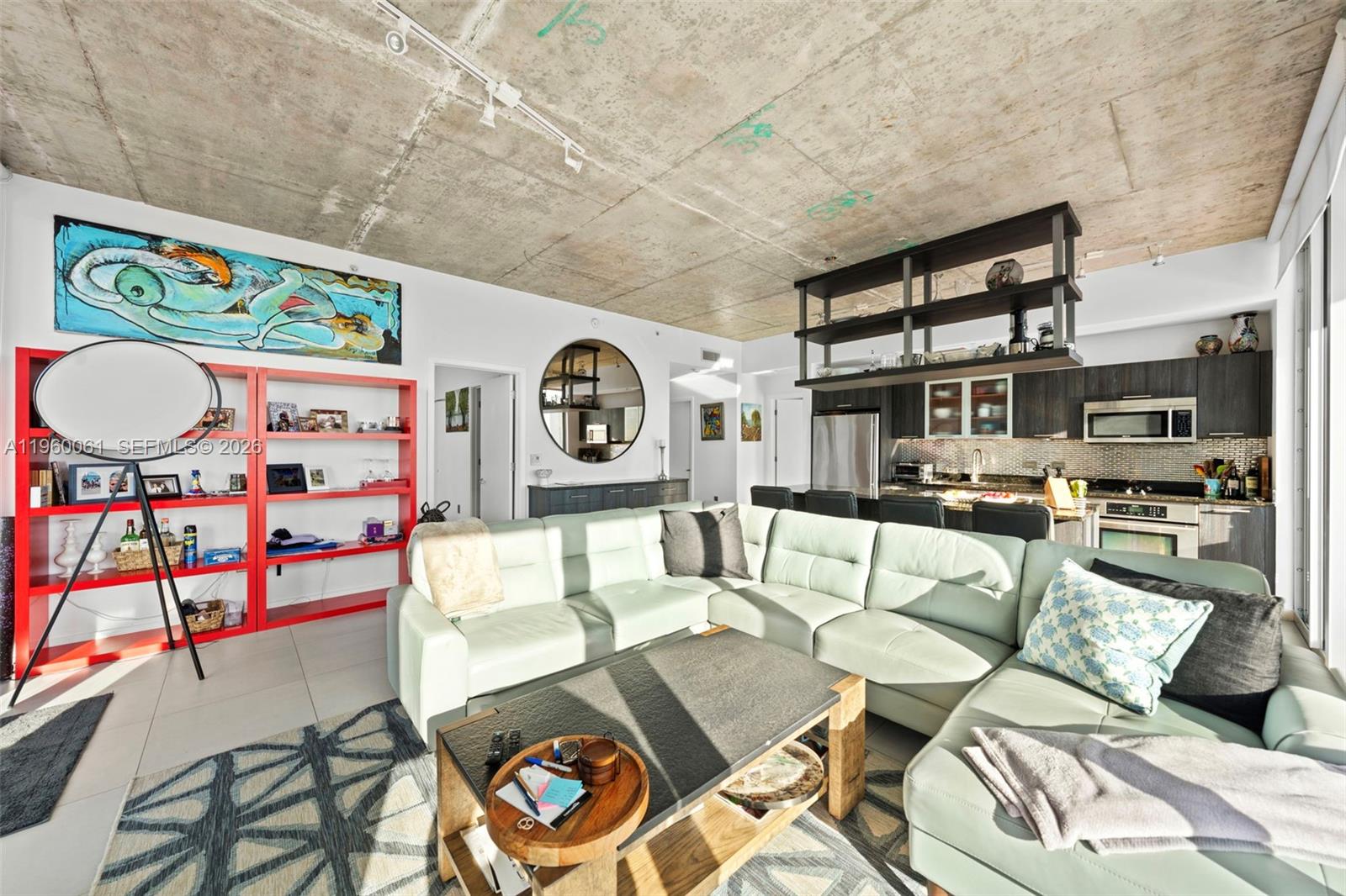 An open-concept living room features a concrete ceiling, a light-colored sectional, and a red bookshelf — 3470 E Coast Ave # H2009, Miami FL 33137, MIAMI, FL