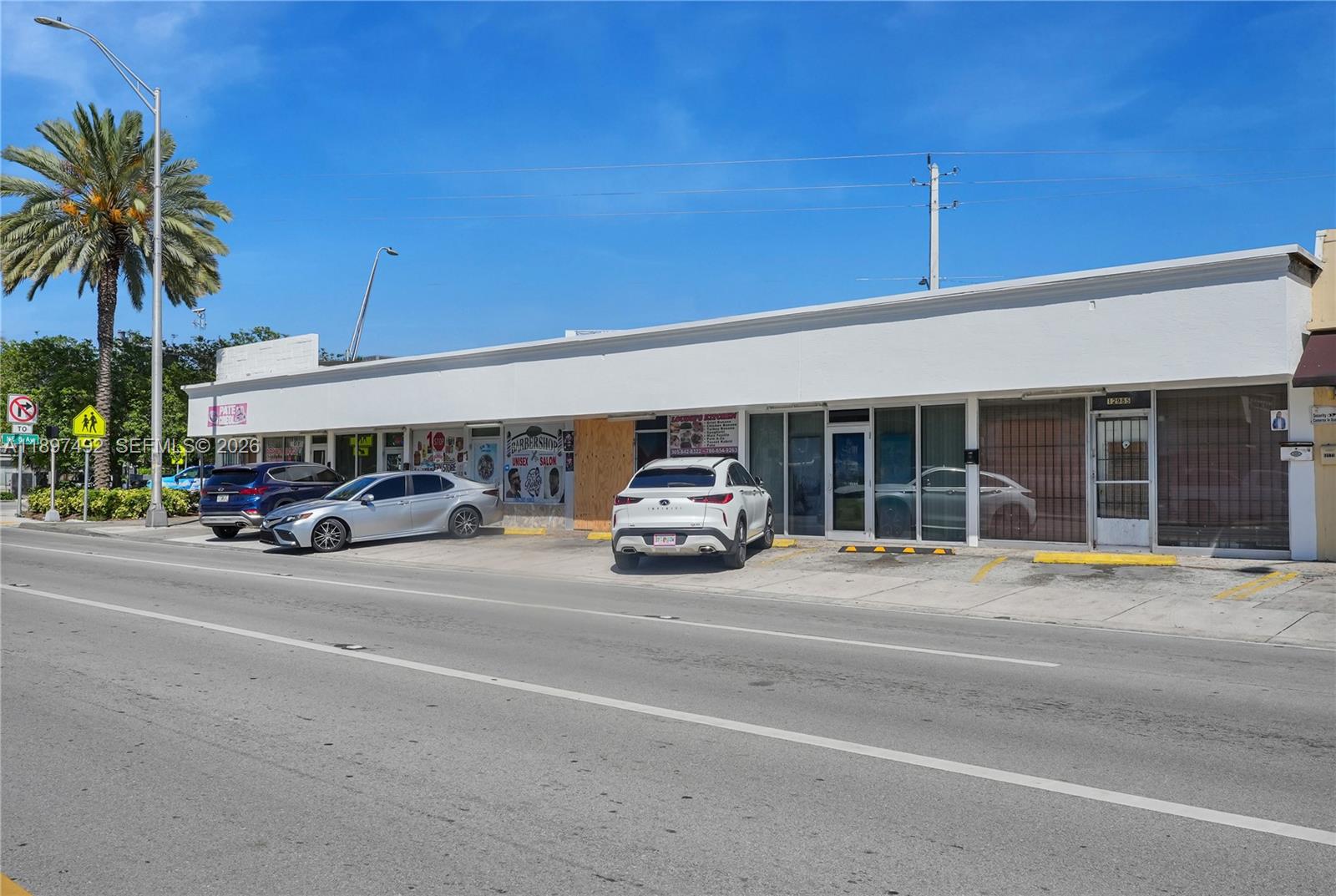 A single-story commercial strip mall with a white facade and parked cars in front — 12985 W Dixie Hwy, North Miami FL 33161, NORTH MIAMI, FL