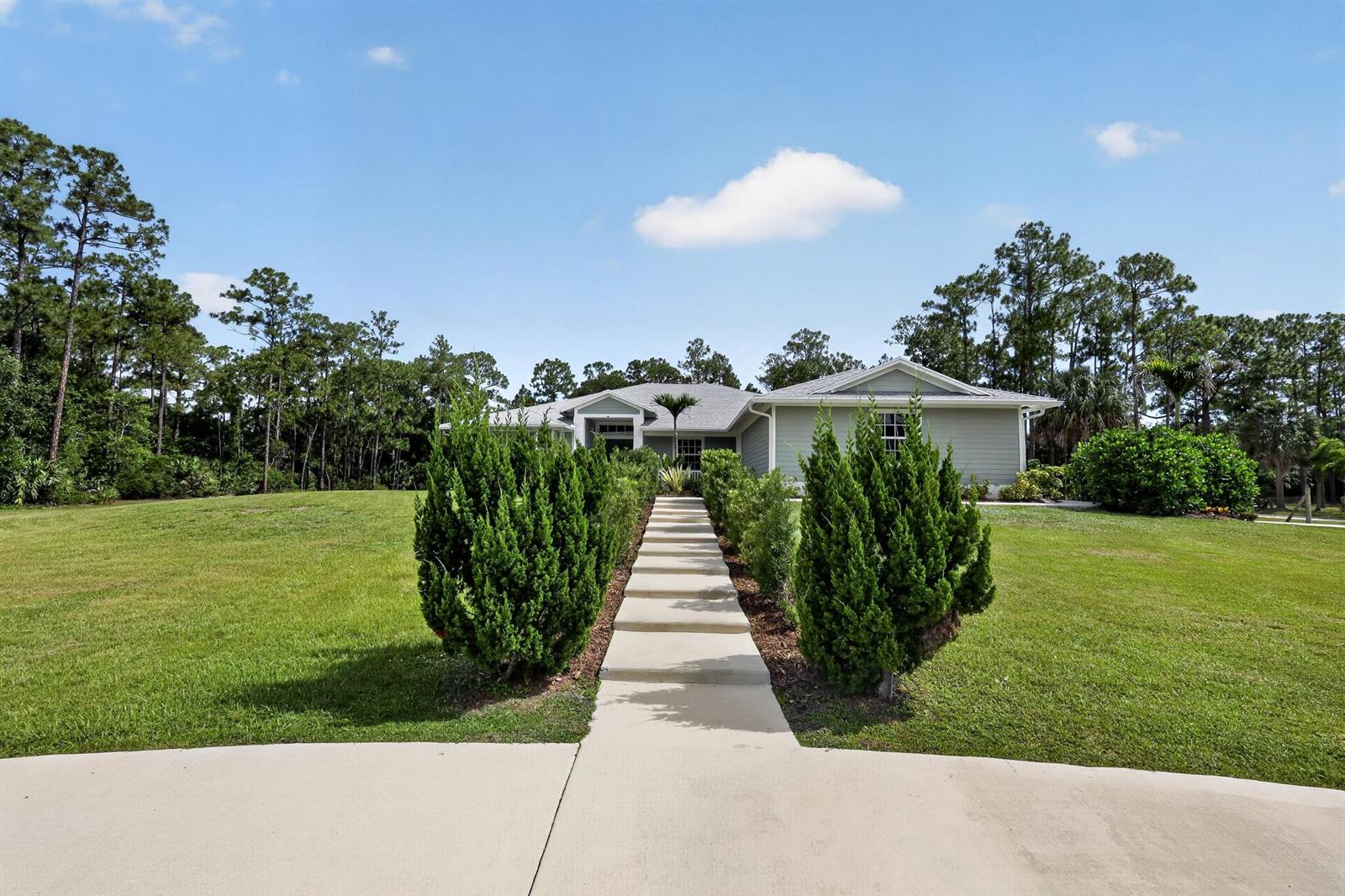 A concrete walkway leads through a grassy yard to the entrance of a suburban house — 11525 157th Place N, Jupiter FL 33478, JUPITER, FL