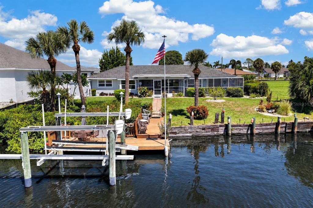 A waterfront house with a boat lift, wooden dock, and American flag in the yard — 2516 DIXON TERRACE, PORT CHARLOTTE, FL