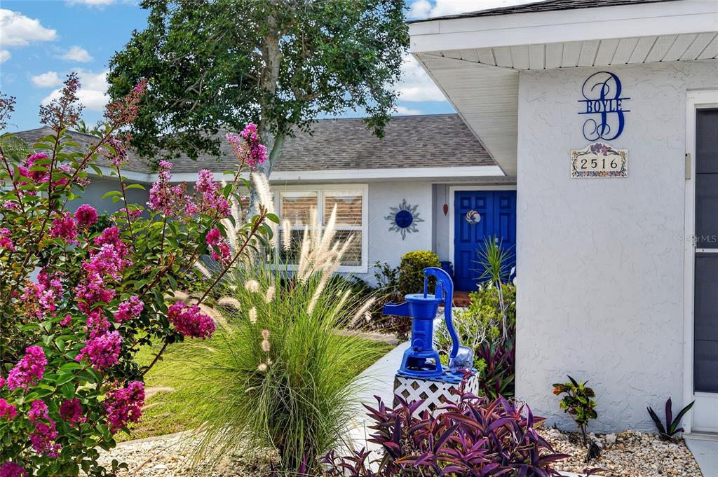 A white house exterior features a blue front door, a decorative water pump, and landscaping — 2516 DIXON TERRACE, PORT CHARLOTTE, FL