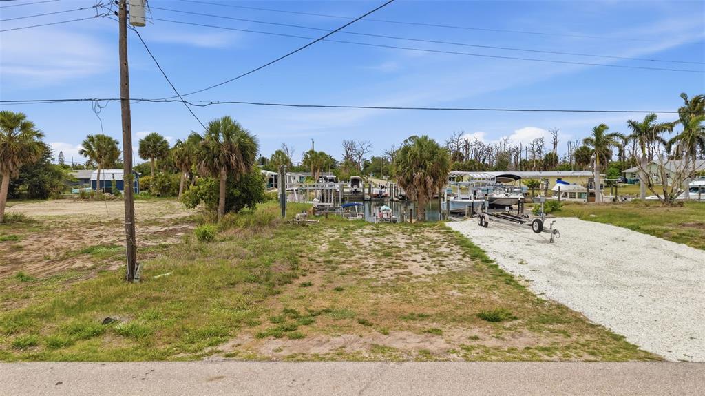 A vacant waterfront lot features a gravel driveway, palm trees, and a private boat slip — 1949 PENNSYLVANIA AVENUE UNIT BL1, ENGLEWOOD, FL