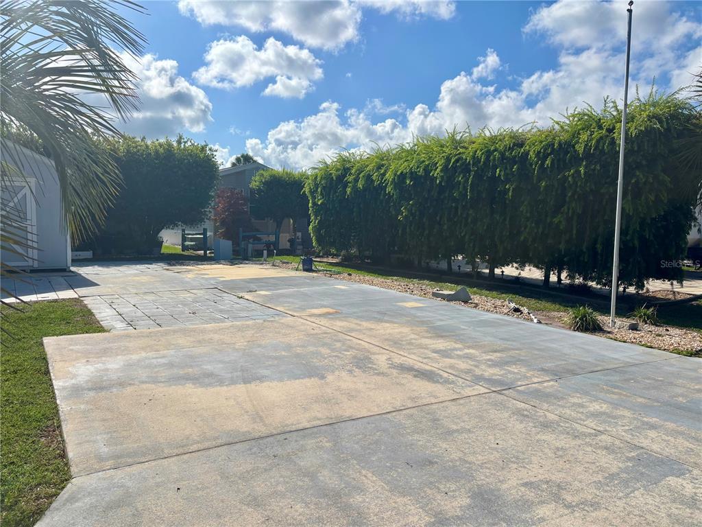 A large concrete driveway sits in front of a tall hedge and a small shed — 3273 NE 102ND AVENUE ROAD, SILVER SPRINGS, FL