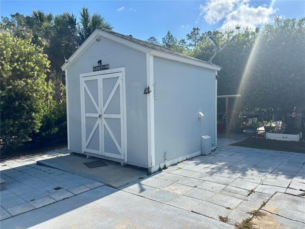 A light blue storage shed with white trim and double doors sits on a patio — 3273 NE 102ND AVENUE ROAD, SILVER SPRINGS, FL