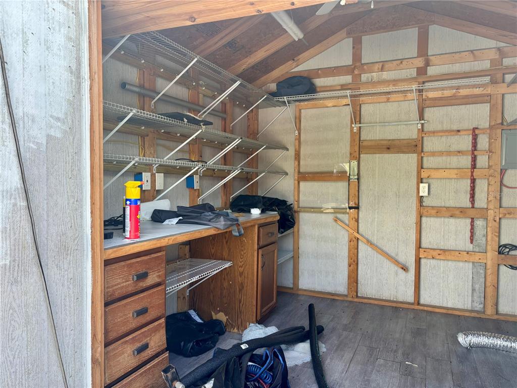 An interior view of a shed featuring wooden wall studs, wire shelving, and a workbench — 3273 NE 102ND AVENUE ROAD, SILVER SPRINGS, FL