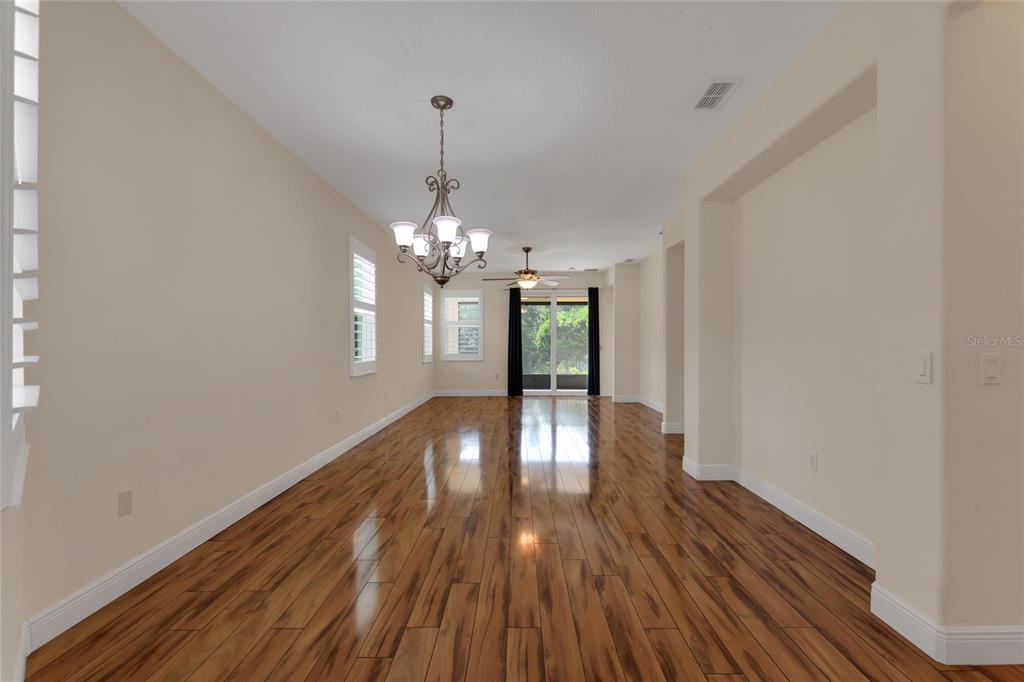 A long, empty room features hardwood floors, a chandelier, and sliding glass doors to outside — 624 GRAND CANAL DRIVE, KISSIMMEE, FL