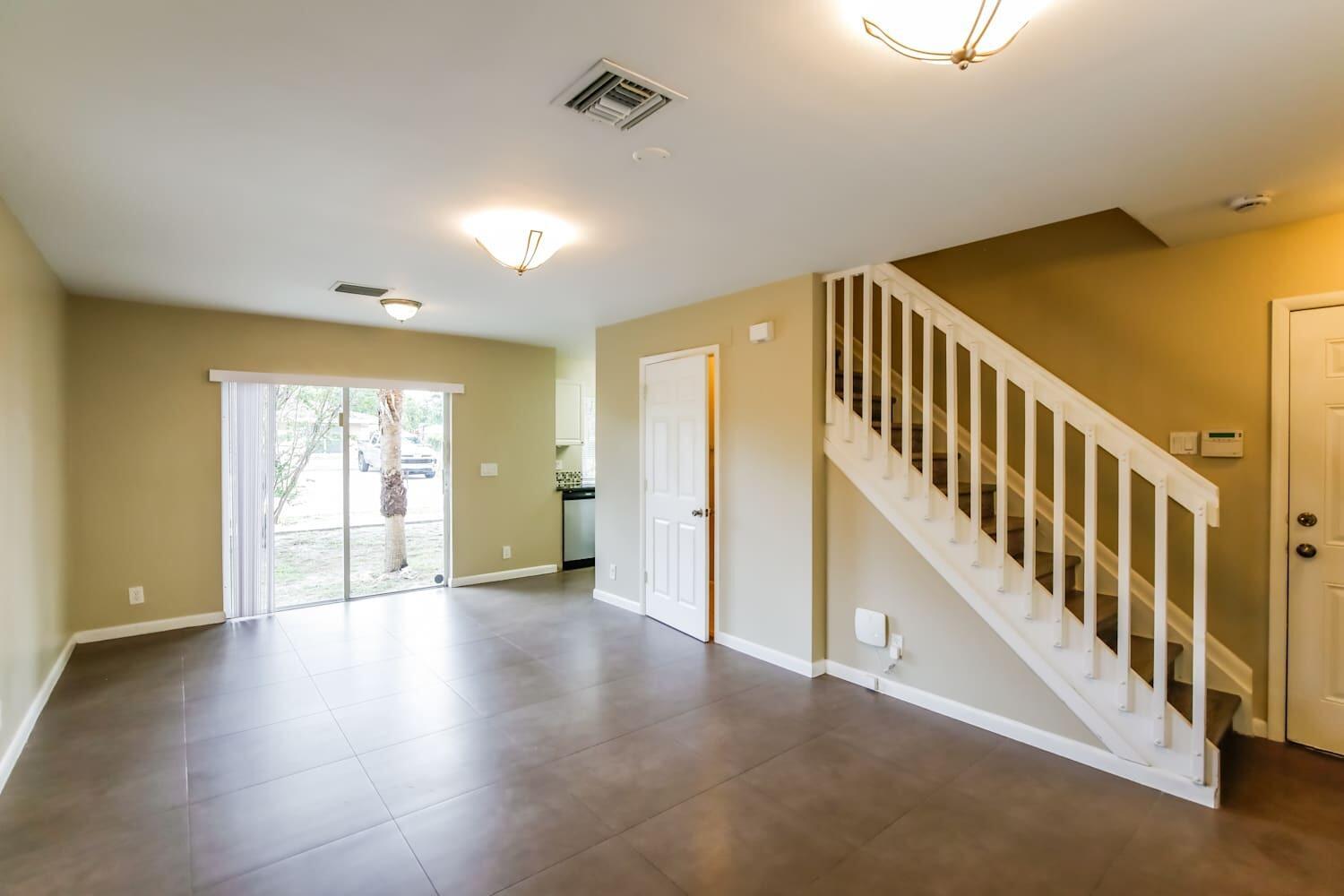 An open living area features tile flooring, a staircase with white railings, and sliding glass doors — DEERFIELD BEACH, FL