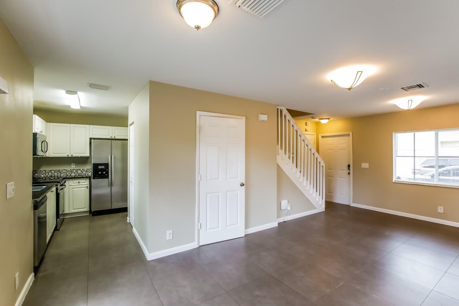 A kitchen with white cabinets and stainless steel appliances opens to a living area — DEERFIELD BEACH, FL