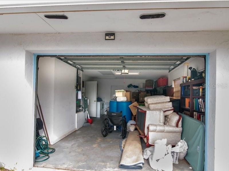 A garage interior contains a wheelchair, stacked furniture, a blue barrel, and various storage items — 1 WESTCLIFFE LANE, PALM COAST, FL