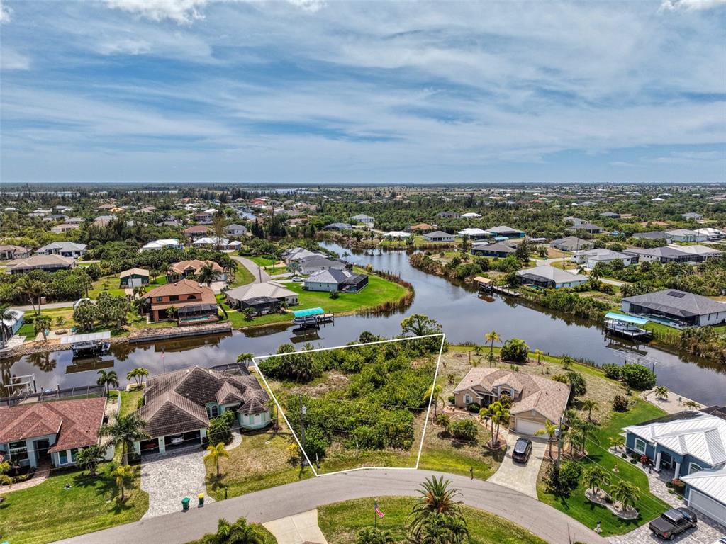 An aerial view shows a vacant residential lot situated between two houses along a canal — 15304 HENNIPEN CIRCLE, PORT CHARLOTTE, FL