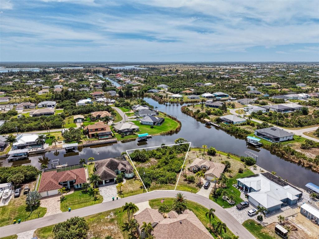 An aerial view shows a vacant waterfront lot outlined in white within a residential neighborhood — 15304 HENNIPEN CIRCLE, PORT CHARLOTTE, FL