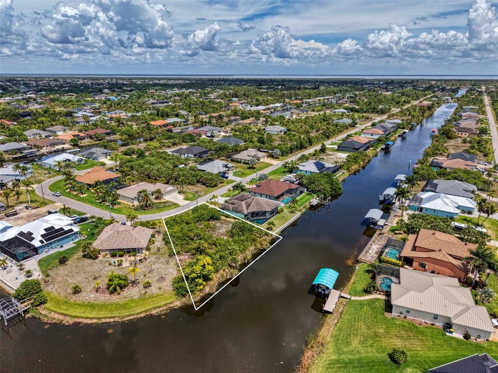An aerial view shows a vacant, trapezoidal waterfront lot situated between two houses along a canal — 15304 HENNIPEN CIRCLE, PORT CHARLOTTE, FL
