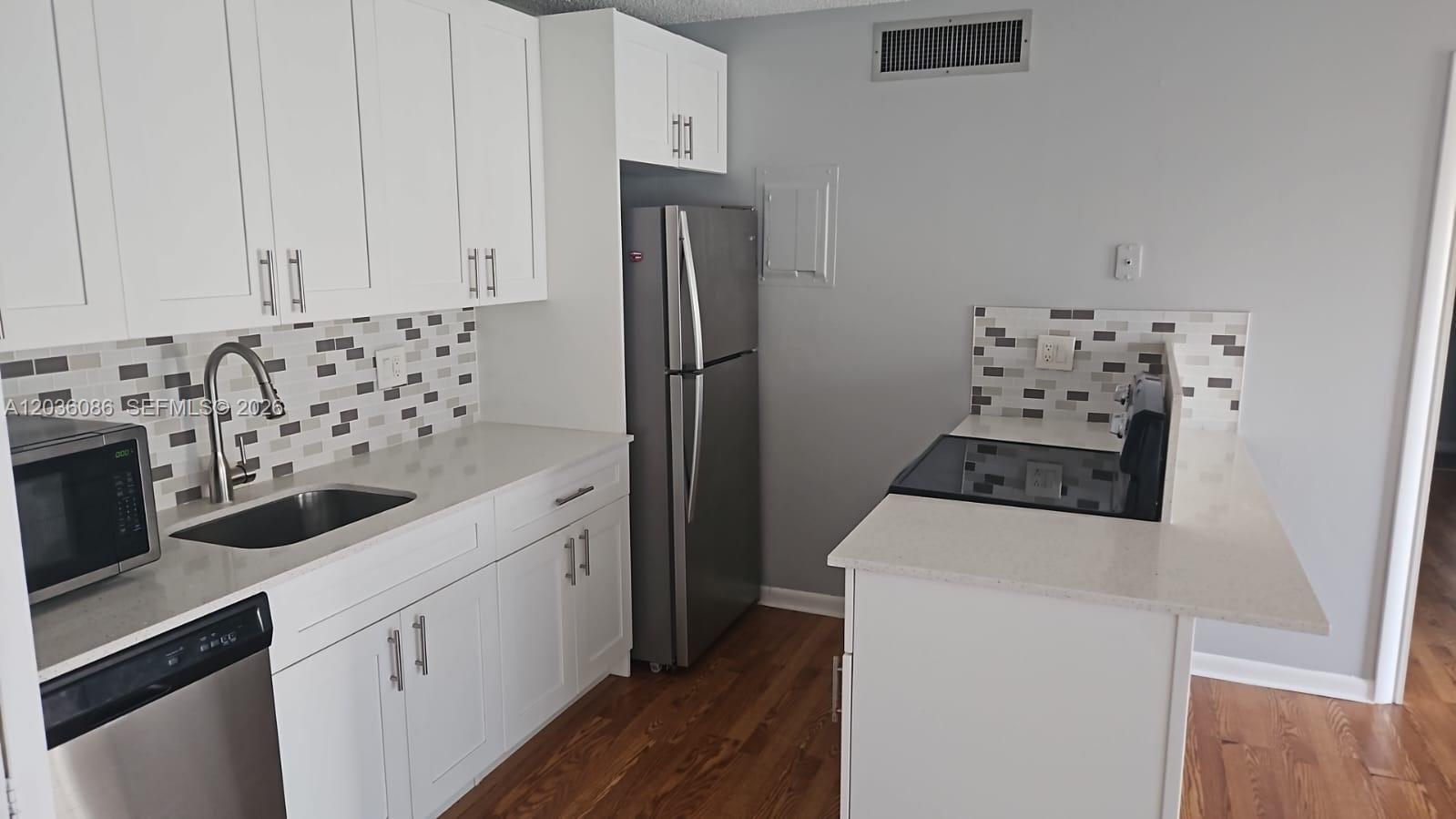 A kitchen features white cabinets, stainless steel appliances, a tiled backsplash, and light-colored countertops — WEST PALM BEACH, FL