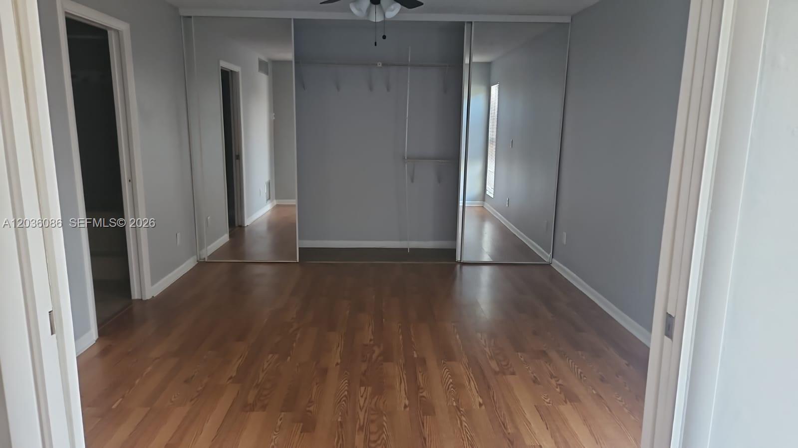A bedroom features light gray walls, wood-look flooring, and a closet with mirrored sliding doors — WEST PALM BEACH, FL