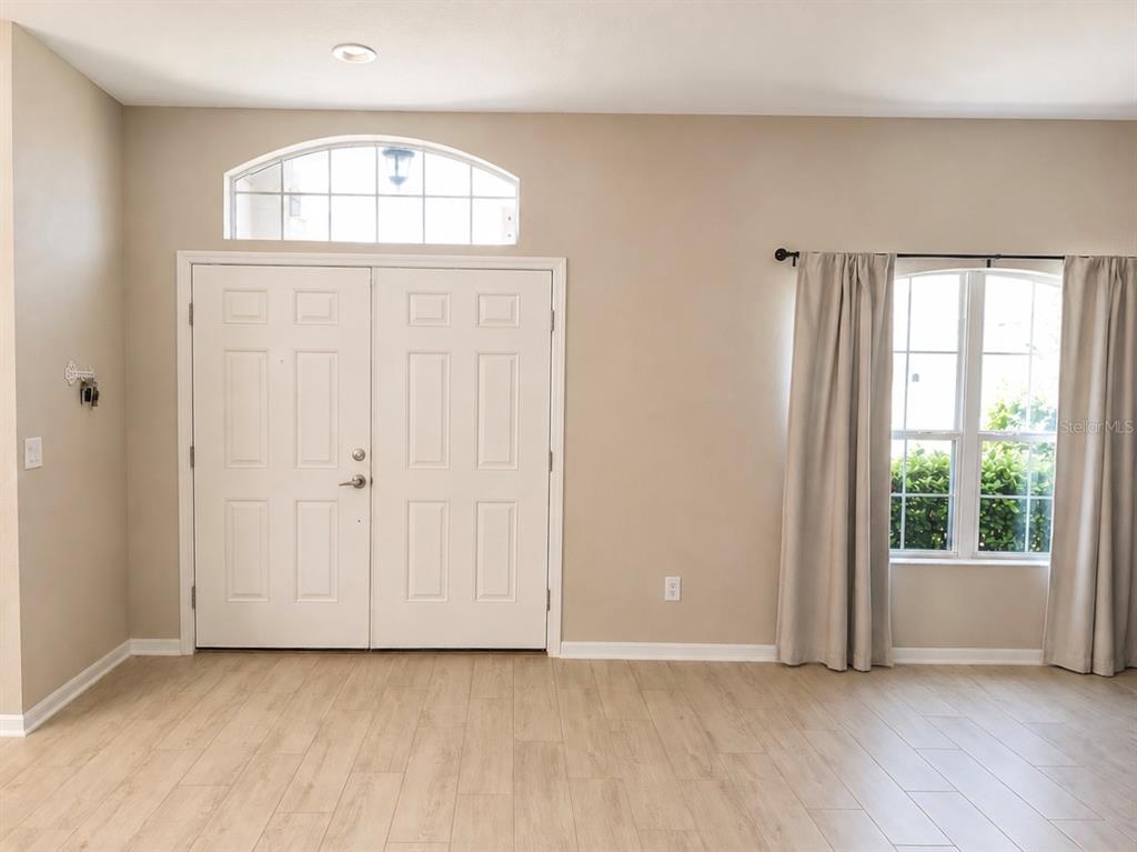 A room with light wood-look flooring, double front doors, and a window with curtains — 4539 CALUMET DRIVE, ST CLOUD, FL