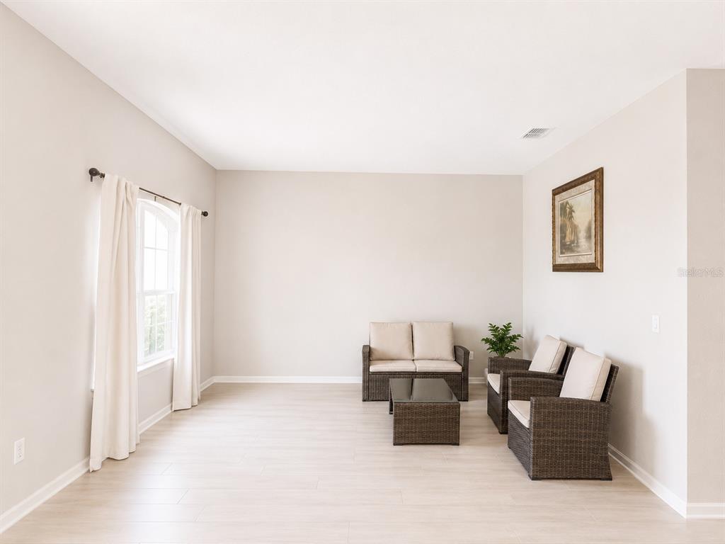 A living room features light wood-look flooring, neutral walls, and wicker-style patio furniture — 4539 CALUMET DRIVE, ST CLOUD, FL