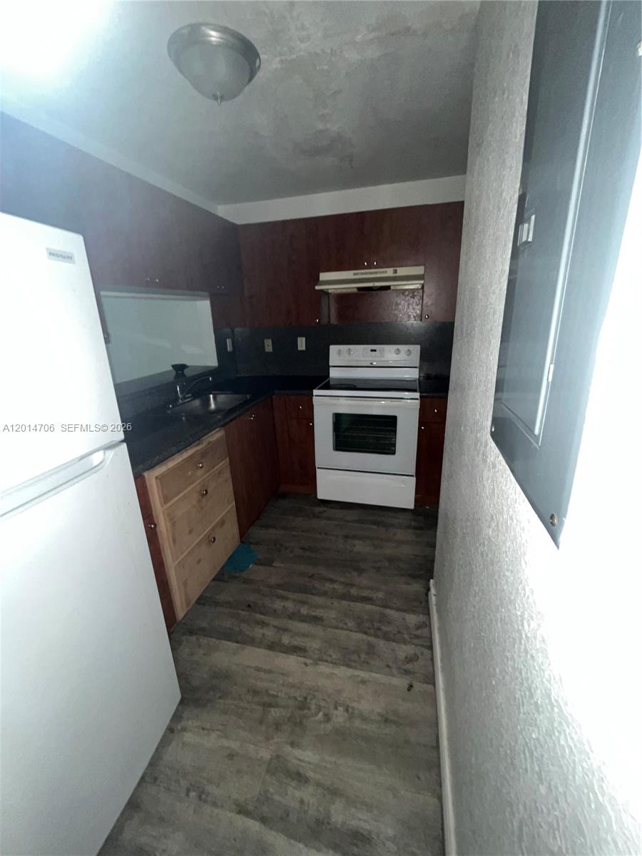 This kitchen features dark wood cabinetry, a white stove, a refrigerator, and wood-look flooring — 2286 NW 136th Ter # 0, Opa-Locka FL 33054, OPA-LOCKA, FL