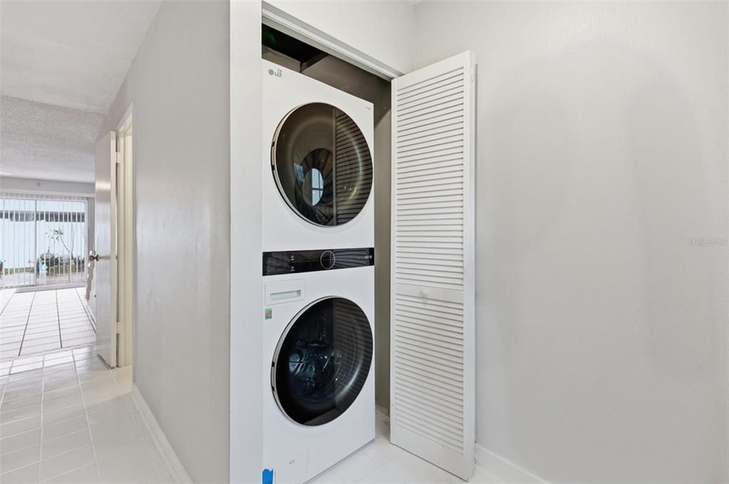 A white stacked washer and dryer unit sits in a closet next to a hallway — 16143 RAMBLING VINE DRIVE E, TAMPA, FL