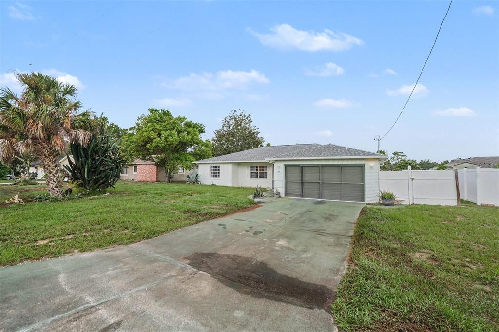A single-story white brick house features a gray garage door and a concrete driveway — 4233 DRISTOL AVENUE, SPRING HILL, FL