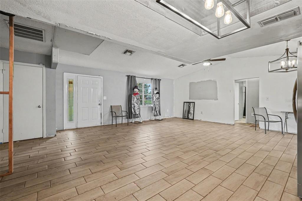 A spacious room with light wood-look tile flooring, white walls, and two hanging light fixtures — 4233 DRISTOL AVENUE, SPRING HILL, FL