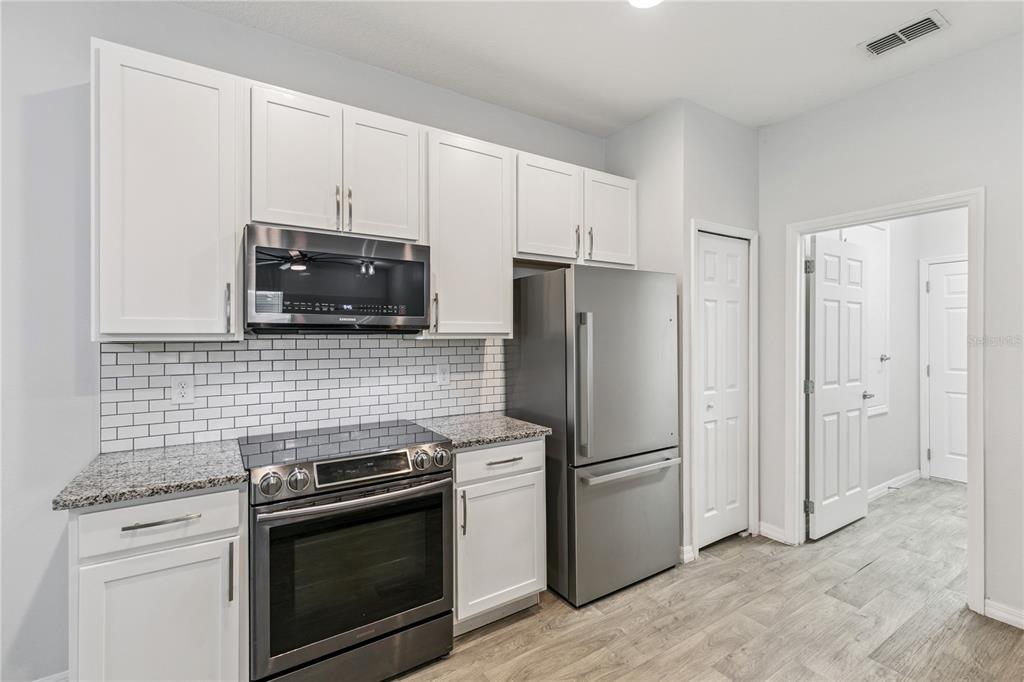 A kitchen features white cabinets, stainless steel appliances, granite countertops, and a white subway tile backsplash — 1863 SHUMARD AVENUE UNIT 1863, ST CLOUD, FL