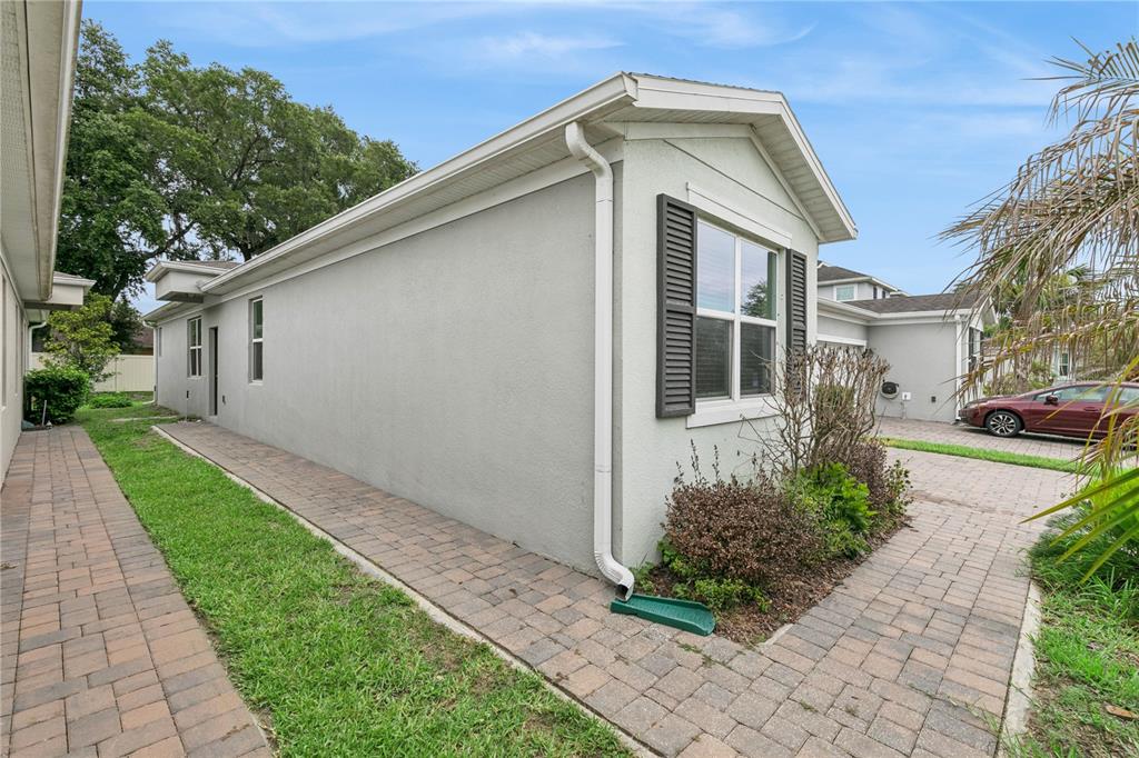 The exterior side view of a gray house features a paved walkway and downspout — 1863 SHUMARD AVENUE UNIT 1863, ST CLOUD, FL