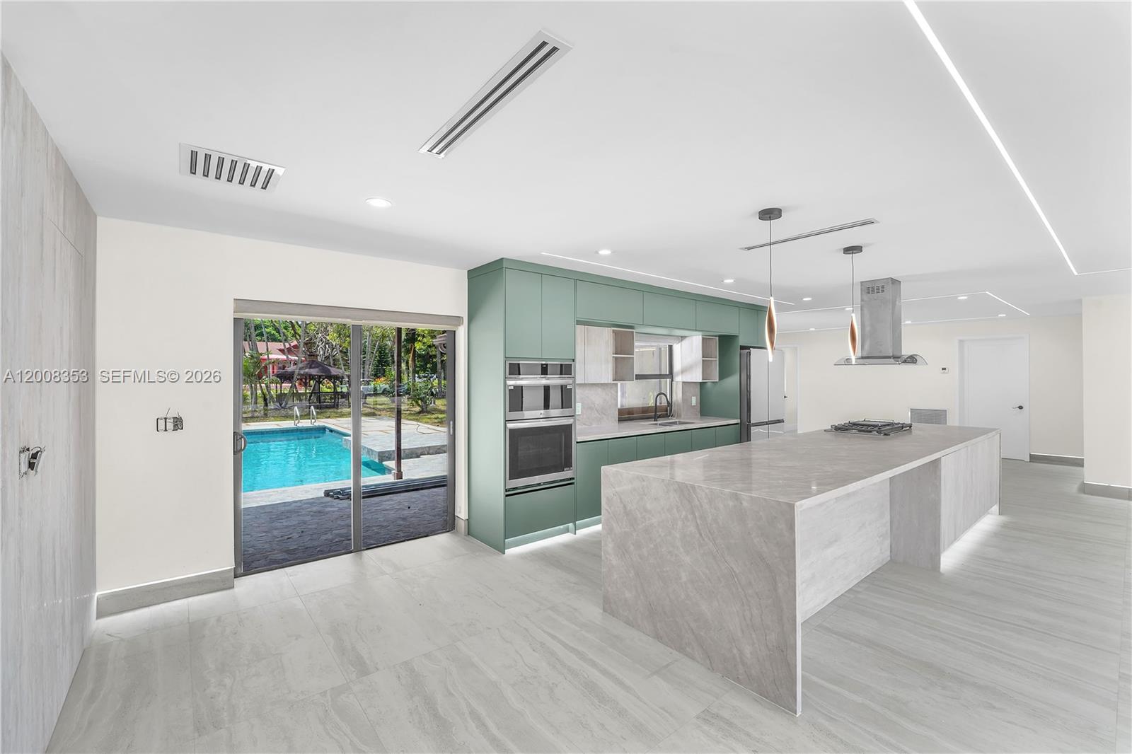 A modern kitchen features sage green cabinetry, a large stone island, and a sliding glass door — 4700 SW 110th Ave, Davie FL 33328, DAVIE, FL
