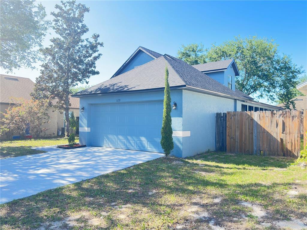 A blue house with a two-car garage and a wooden fence on a sunny day — 1133 OLYMPIC COURT, APOPKA, FL