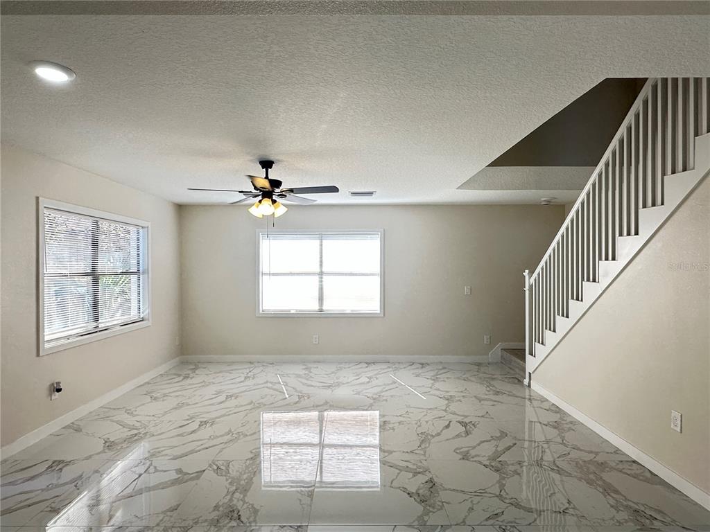 A living room features white marble-look tile flooring, a ceiling fan, and a staircase — 1133 OLYMPIC COURT, APOPKA, FL