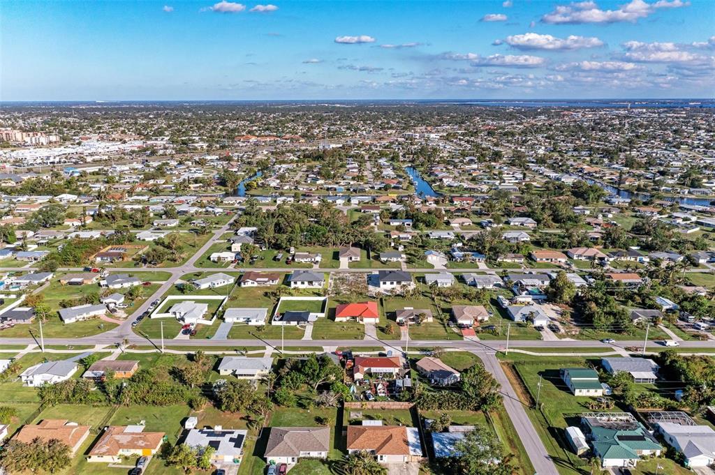 An aerial view shows a residential neighborhood with single-family homes, streets, and green lawns — 3332 ELKCAM BOULEVARD, PORT CHARLOTTE, FL