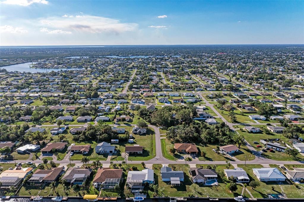 An aerial view shows a suburban neighborhood with houses along a canal under a blue sky — 3332 ELKCAM BOULEVARD, PORT CHARLOTTE, FL