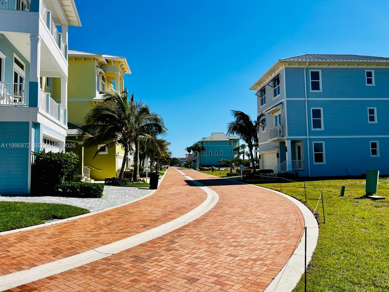 A paved road curves between colorful multi-story houses under a clear blue sky — 4803 Watersong Way, Fort Pierce FL 34949, FORT PIERCE, FL