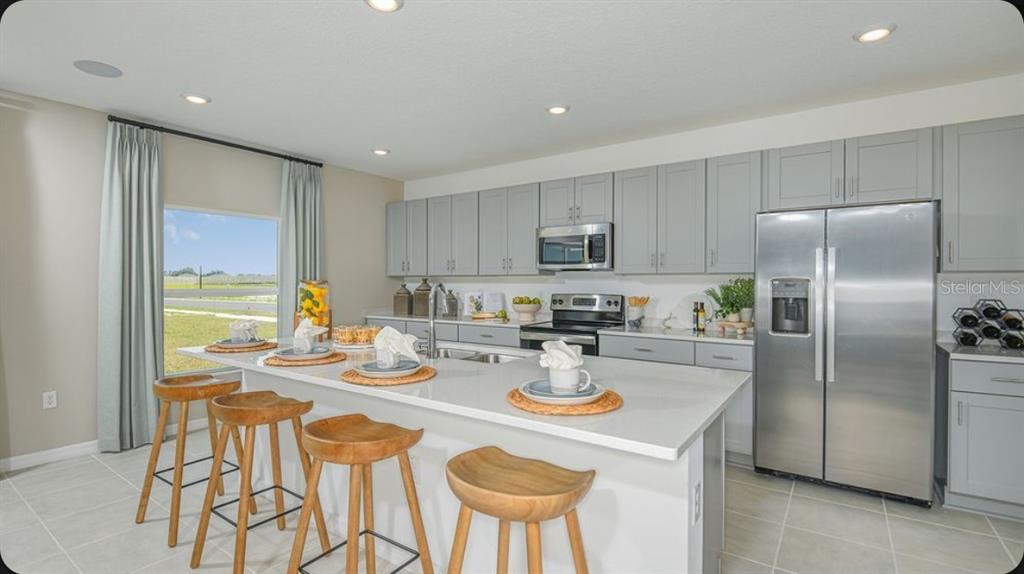 A kitchen features gray cabinets, stainless steel appliances, a white island, and four wooden stools — 6786 EQUINOX LANE, NORTH FORT MYERS, FL