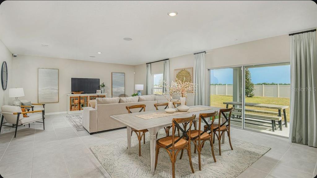 An open-concept living and dining area with tile floors, a large sofa, and sliding doors — 6786 EQUINOX LANE, NORTH FORT MYERS, FL