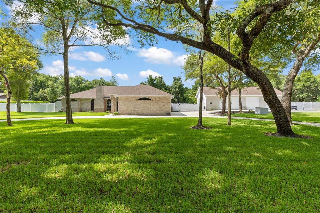A brick house and a detached garage sit on a large, tree-shaded grassy lawn — 713 ERNEST DRIVE, PORT ORANGE, FL