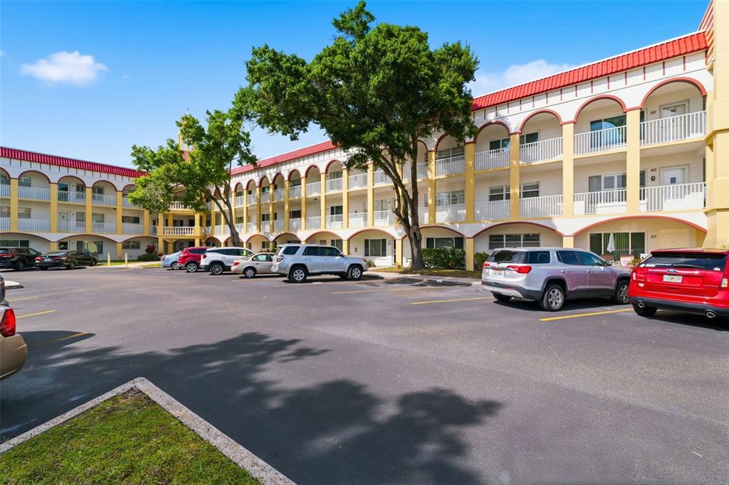 A three-story apartment building with arched balconies and a parking lot in the foreground — 2430 FLORENTINE WAY UNIT 58, CLEARWATER, FL